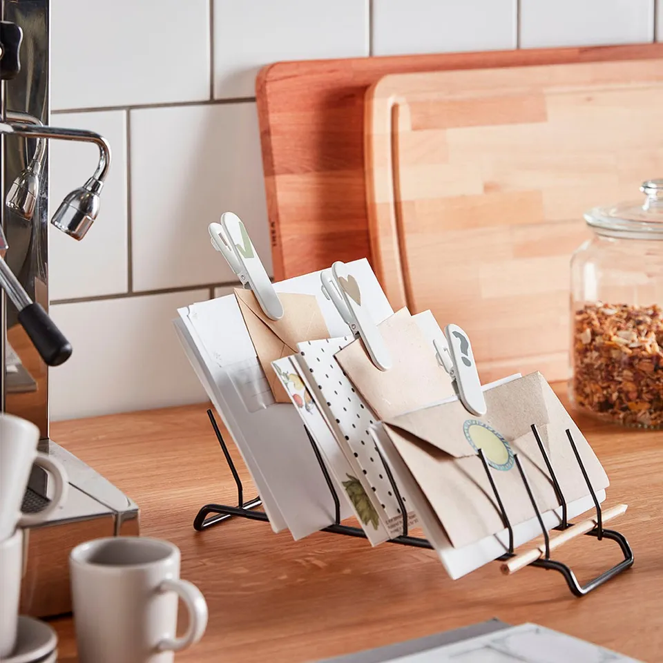 Kitchen counter with black metal card holder holding assorted cards, next to a coffee machine and jar of coffee beans.