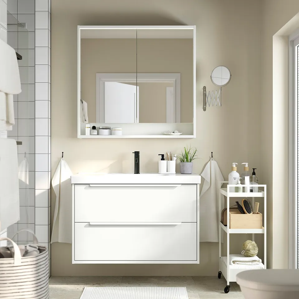 Modern white bathroom with cabinet, sink, mirror, and organiser. Clean, sleek design. Spacious and well-organized.