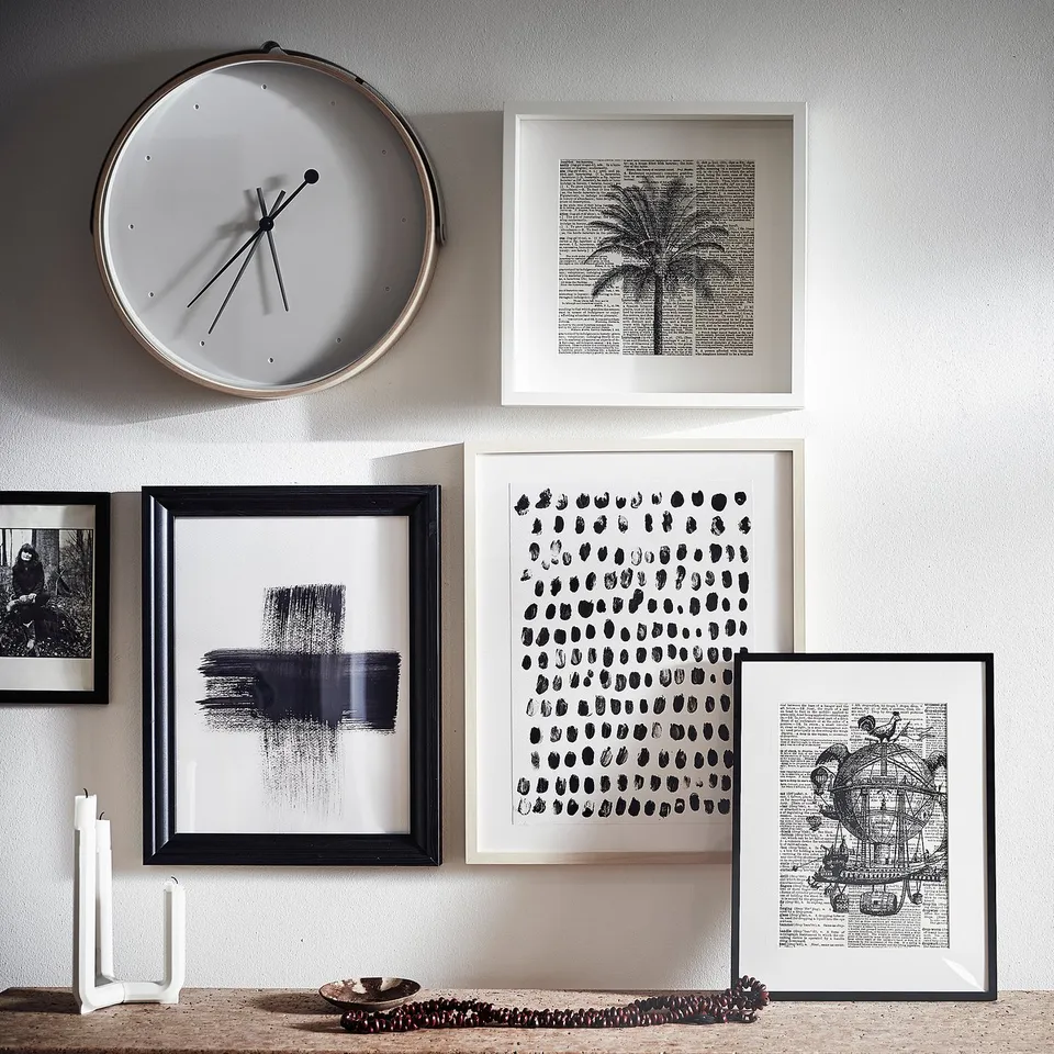 Wall display with white clock, four black & white art prints, and decorative objects. Modern minimalist design.