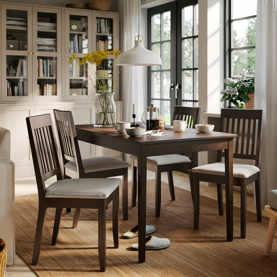 Cosy dining area with NÄSINGE dark wood table & 4 cushioned chairs. Bright windows, flowers, bookshelf backdrop.