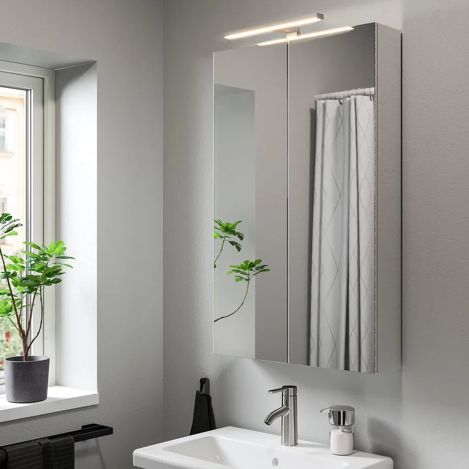 Modern bathroom with VÅTHULT wall lamp above sink, large mirror, white towel, and plant.