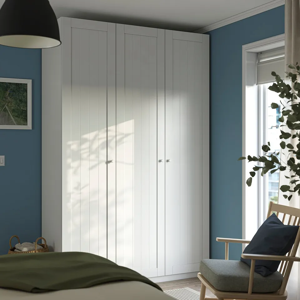 Serene bedroom with PAX wardrobe, wooden chair, and plant by window.