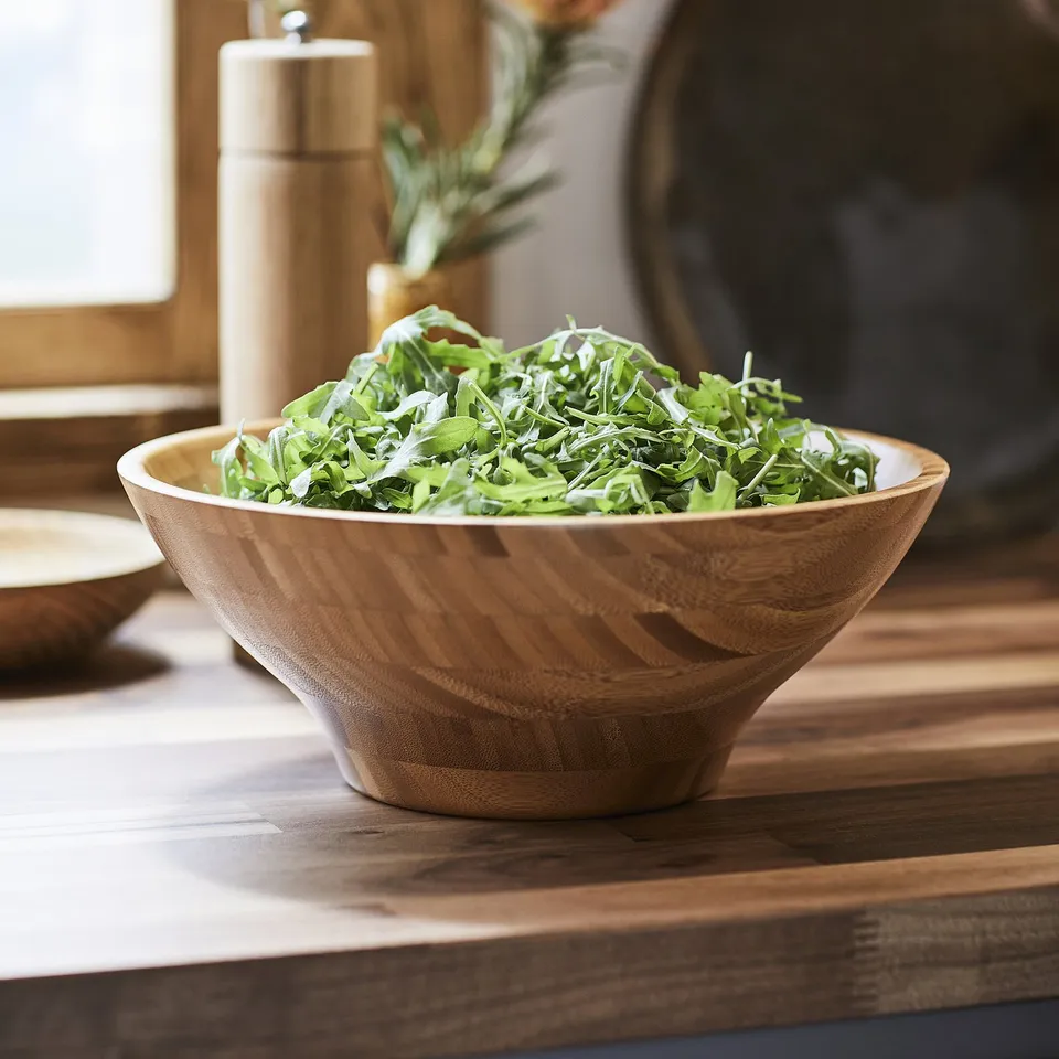 Bowl of fresh greens in a stylish wooden bowl on a wooden table.