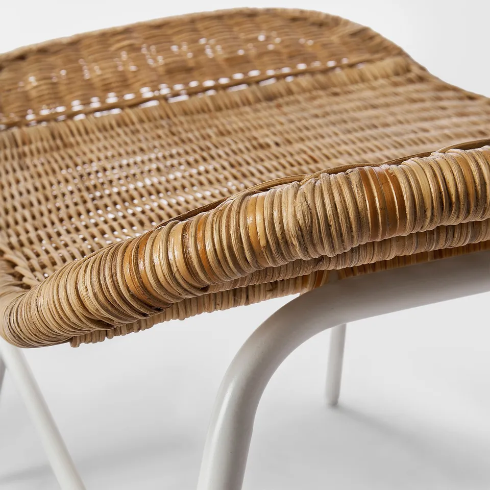 Handwoven rattan stool, showcasing intricate, natural weave and curved edges, supported by white metal legs.