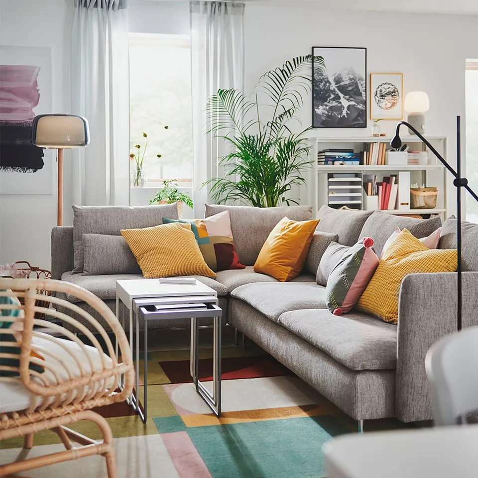 Modern living room with grey SÖDERHAMN sofa, colourful pillows, side tables, plants, and wall art.