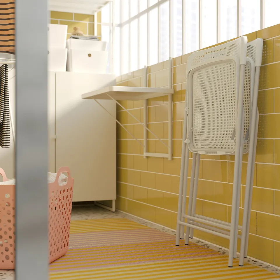 Bright, small room with yellow-tiled walls and striped rug. Includes white plastic folding chair and pink laundry basket.