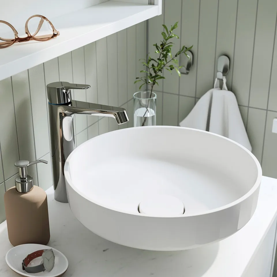 Modern bathroom sink with sleek tap, soap dispenser, small plant, and towel.