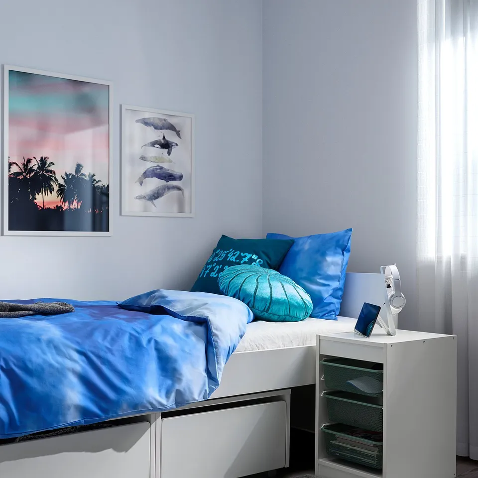 Bedroom with white TROFAST storage, blue bedding, mesh boxes, neat bed, two wall arts.