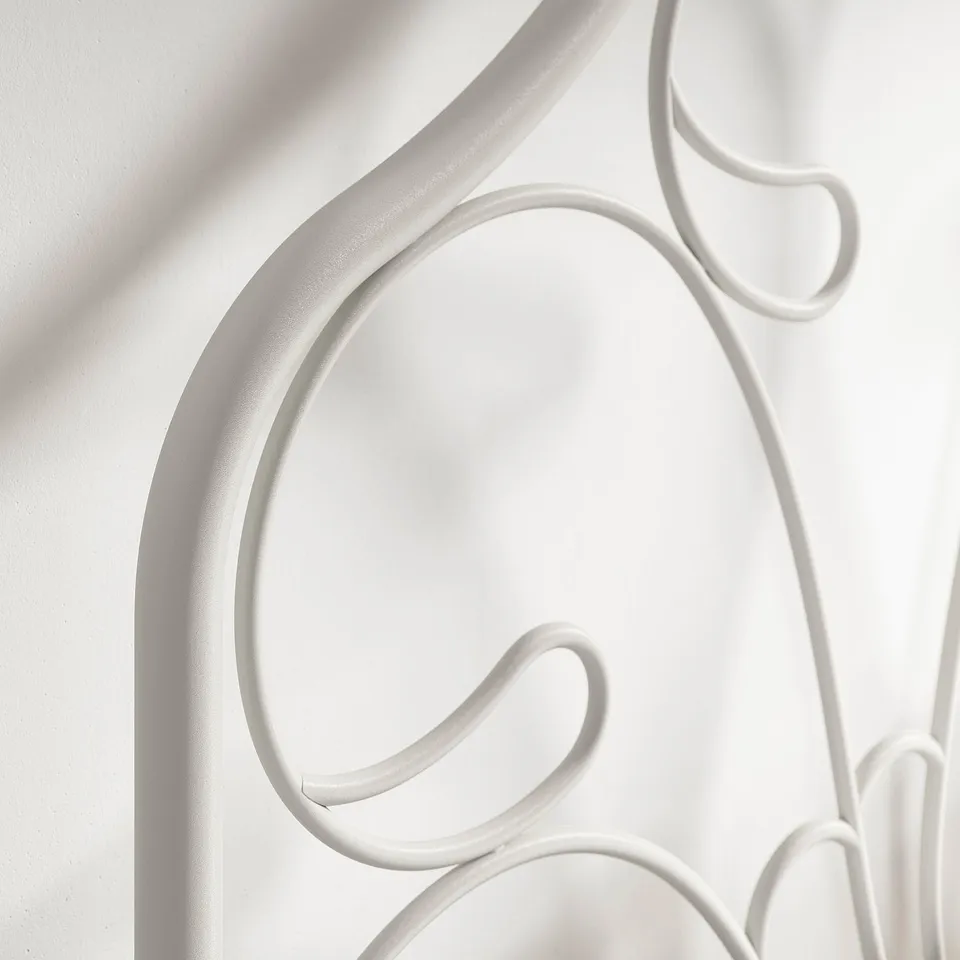 White wrought iron bed frame detail, showcasing intricate curves and sturdy design.