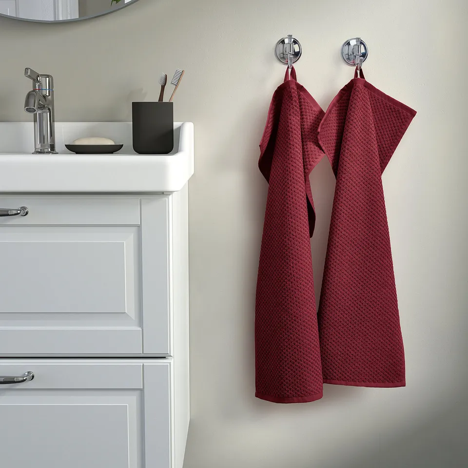 Bathroom with hanging red-grey GULVIAL towels, white cabinet, chrome tap, toothbrush holder.