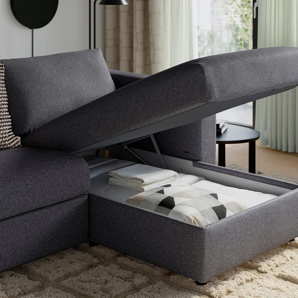 Modern grey sofa with open storage ottoman, showing folded blanket and pillows inside.