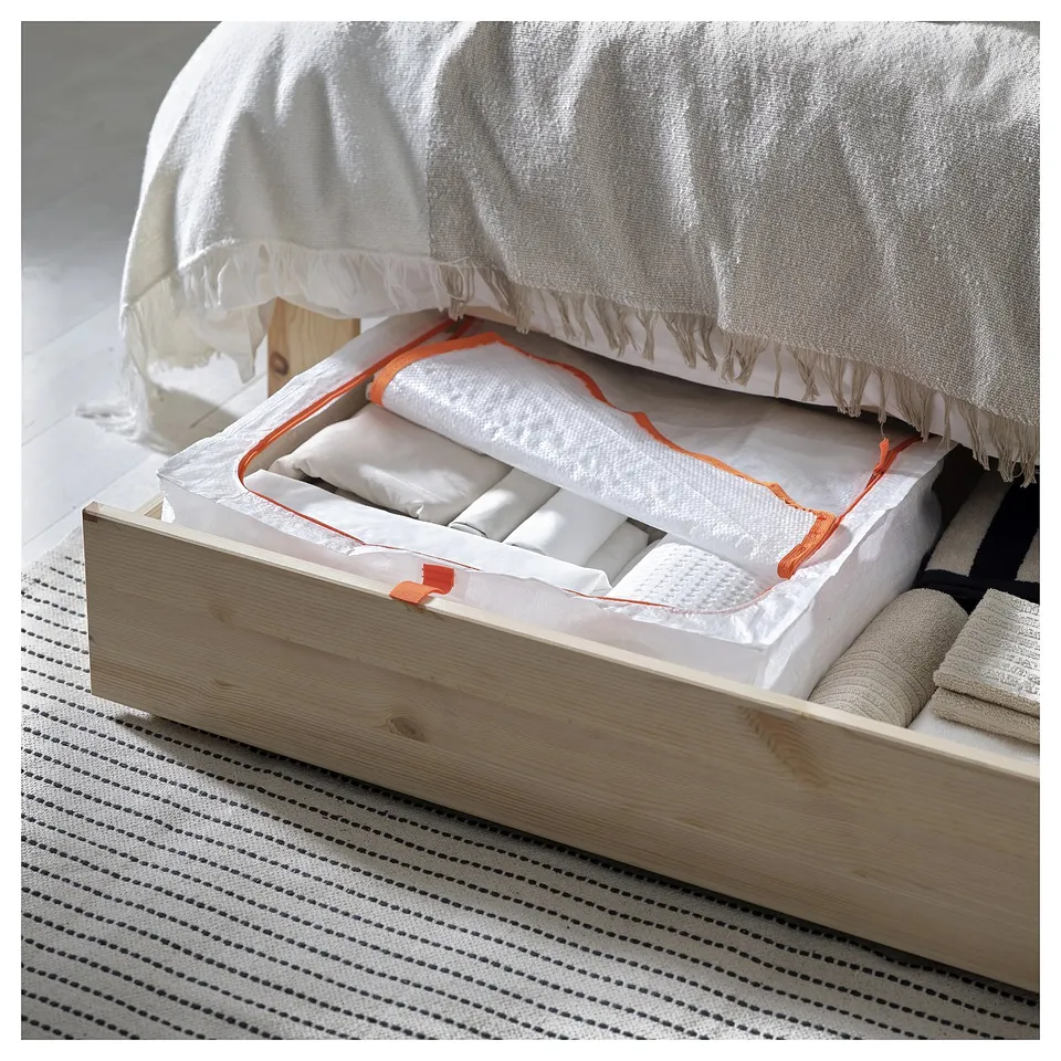 Bed with open drawer showing folded linens, white with orange border, on striped rug.