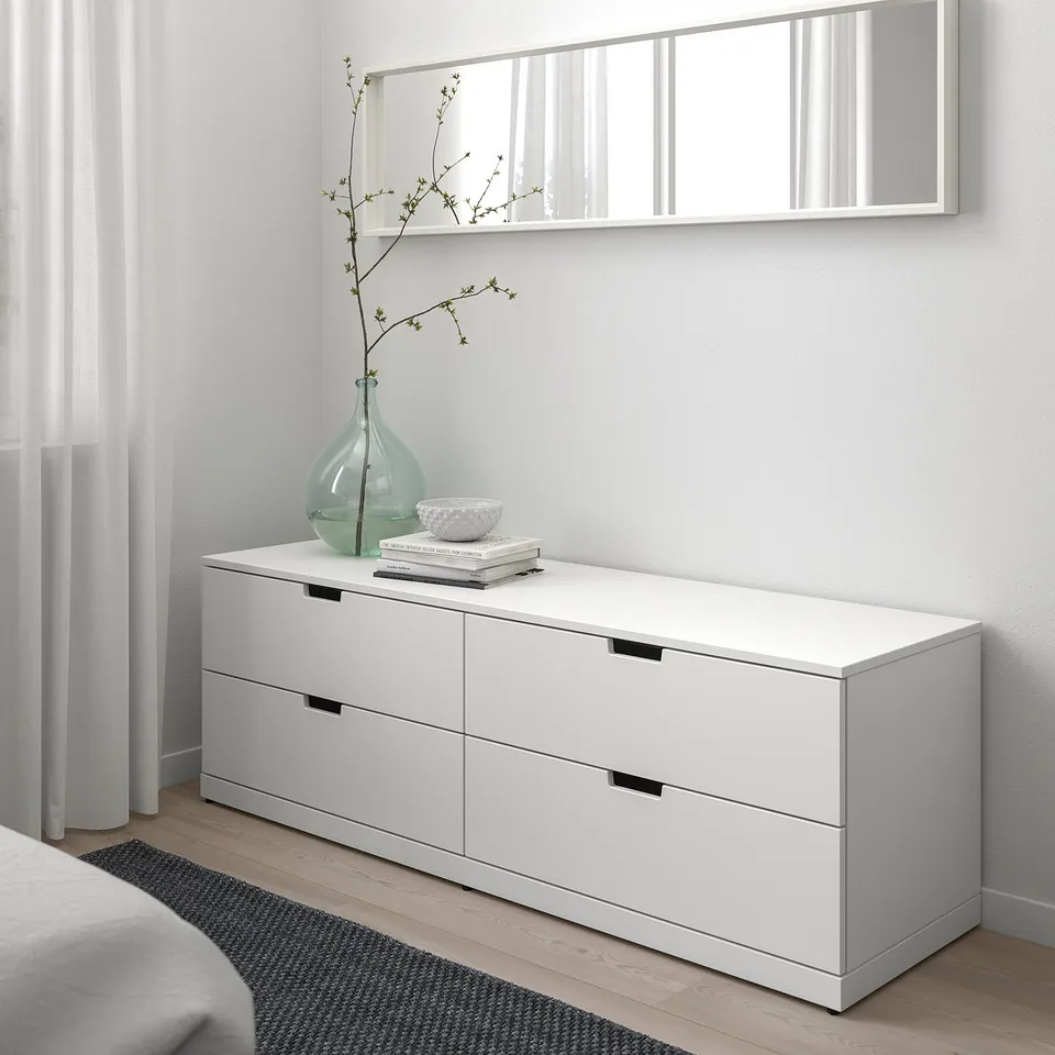 Minimalist bedroom with NORDLI chest, mirror, books, vase, & bed.