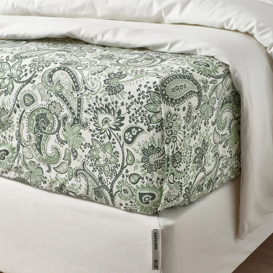 Green paisley sheet with sheen on bed, RODGERSIA tag shows hem.