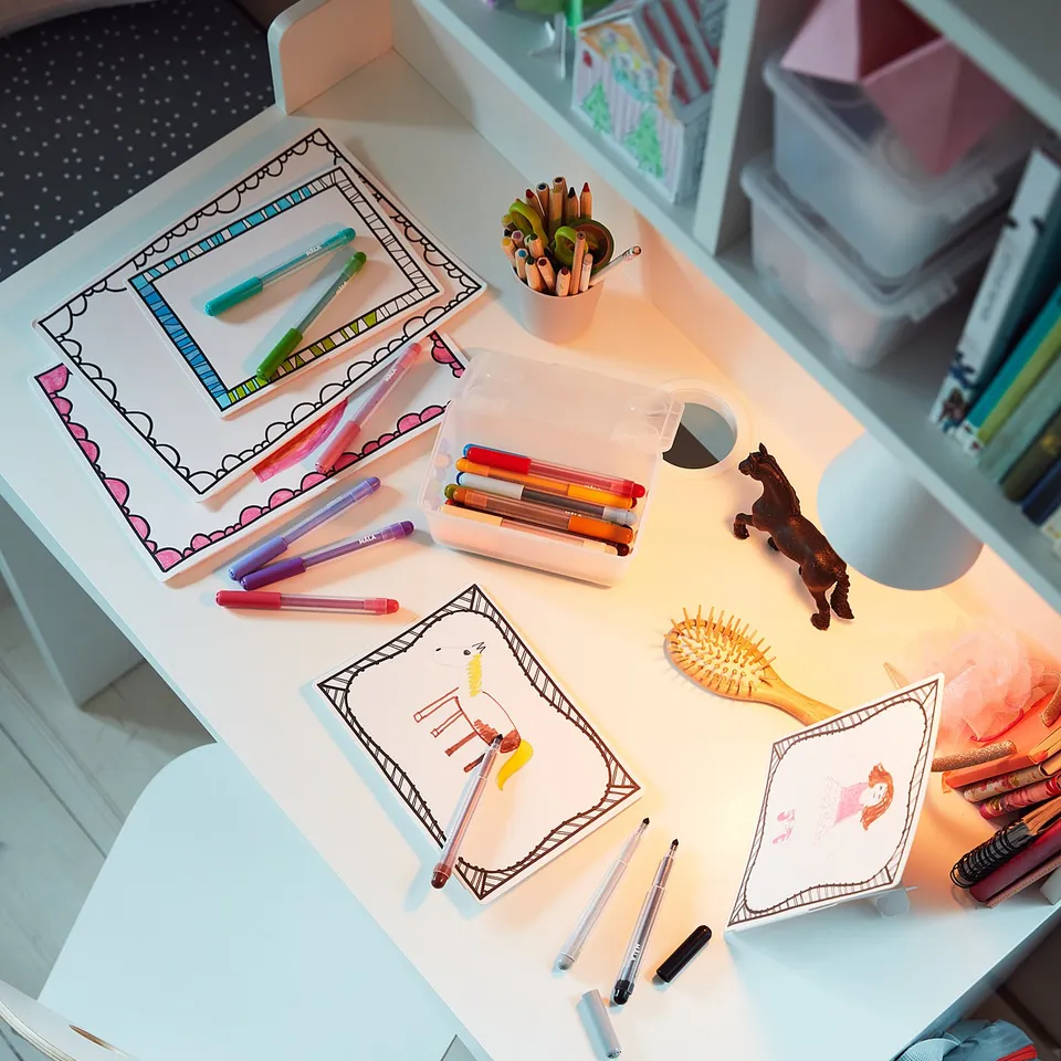 White childrens desk with drawers, filled with colourful arts and crafts supplies.