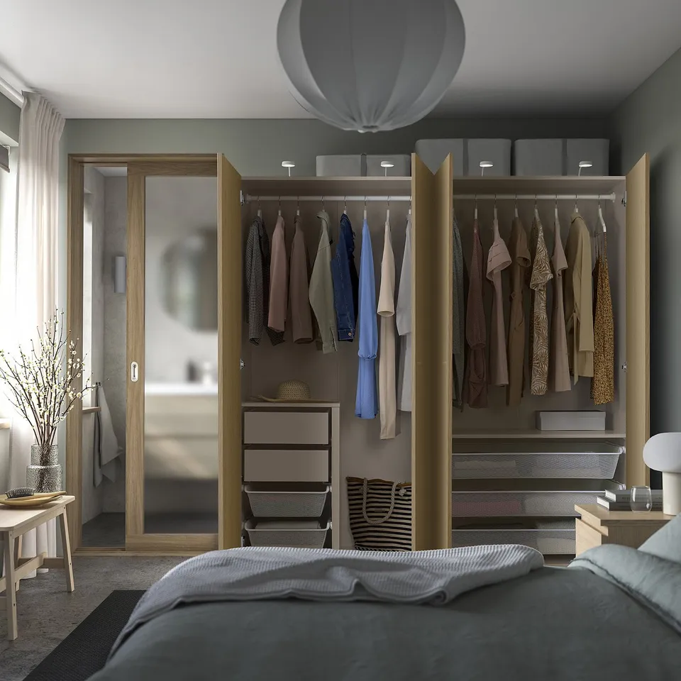 A modern bedroom with an open PAX wardrobe displaying clothes, shelves, and storage baskets.