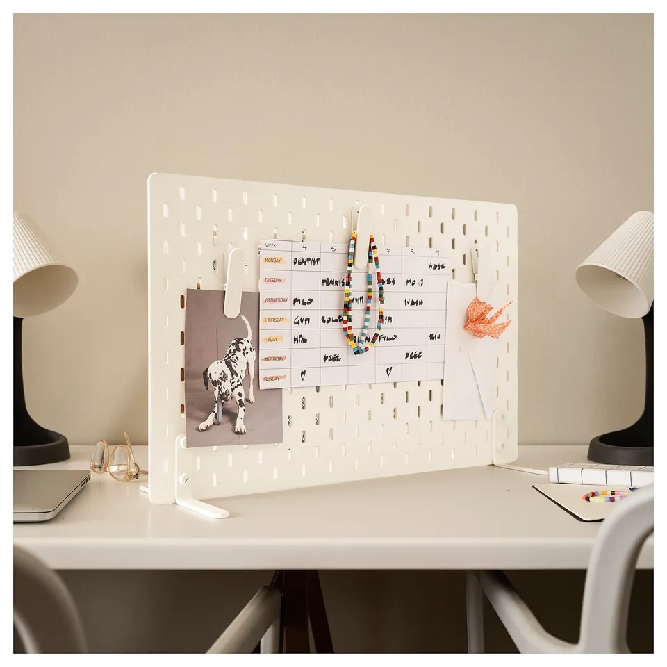 Organised workspace with SKÅDIS white pegboard displaying calendar and notes, flanked by lamps on either side.