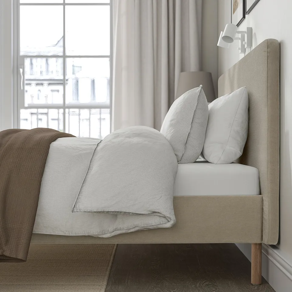 Neutral-toned bed with padded headboard, minting comfort, against a large window. Soft, washable cover enhances durability.