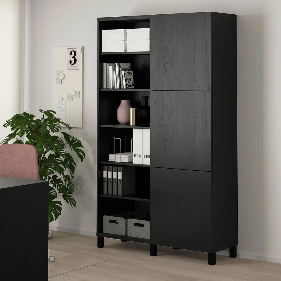Black ikea BESTÅ storage cabinet with open & closed compartments, surrounded by decor and a large plant.