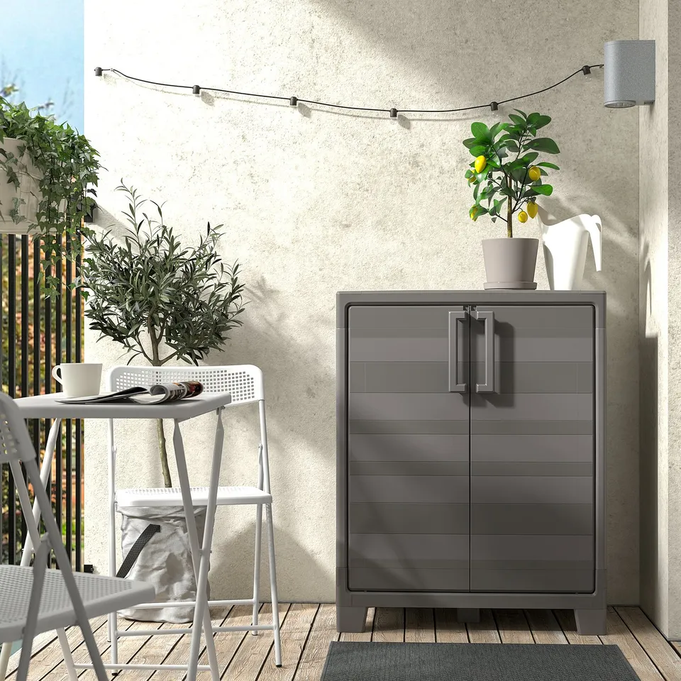 Small white outdoor table & chairs, grey storage cabinet, decorated with plants.