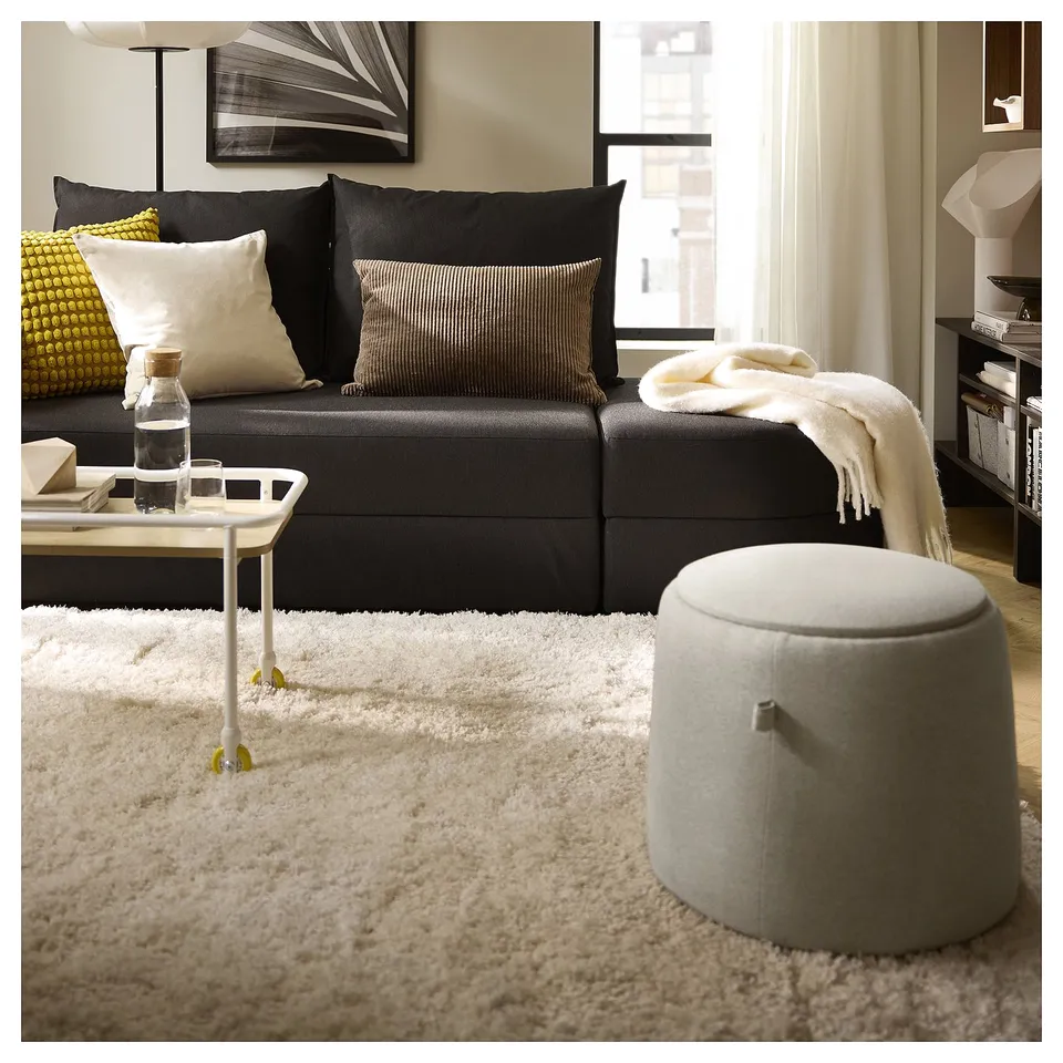 Modern living room with black sofa, white shaggy rug, and striped pillow; minimalist decor.