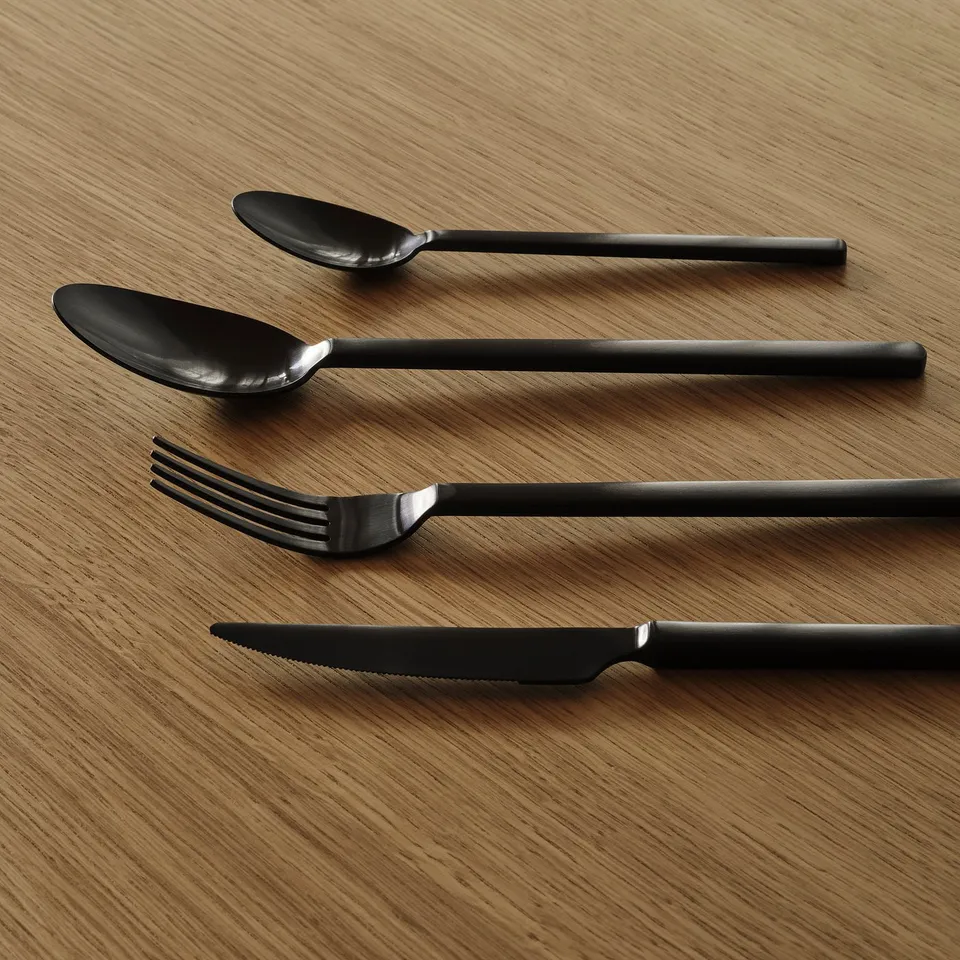 Black-handled cutlery set on wooden table, minimalist design.