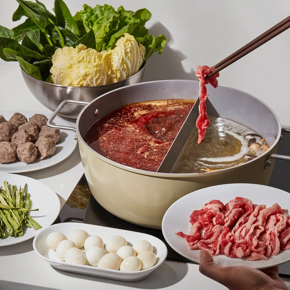 Hot pot setup with SKÄGGTORSK pot, showing different cooking compartments, non-stick surface, and various ingredients around it.