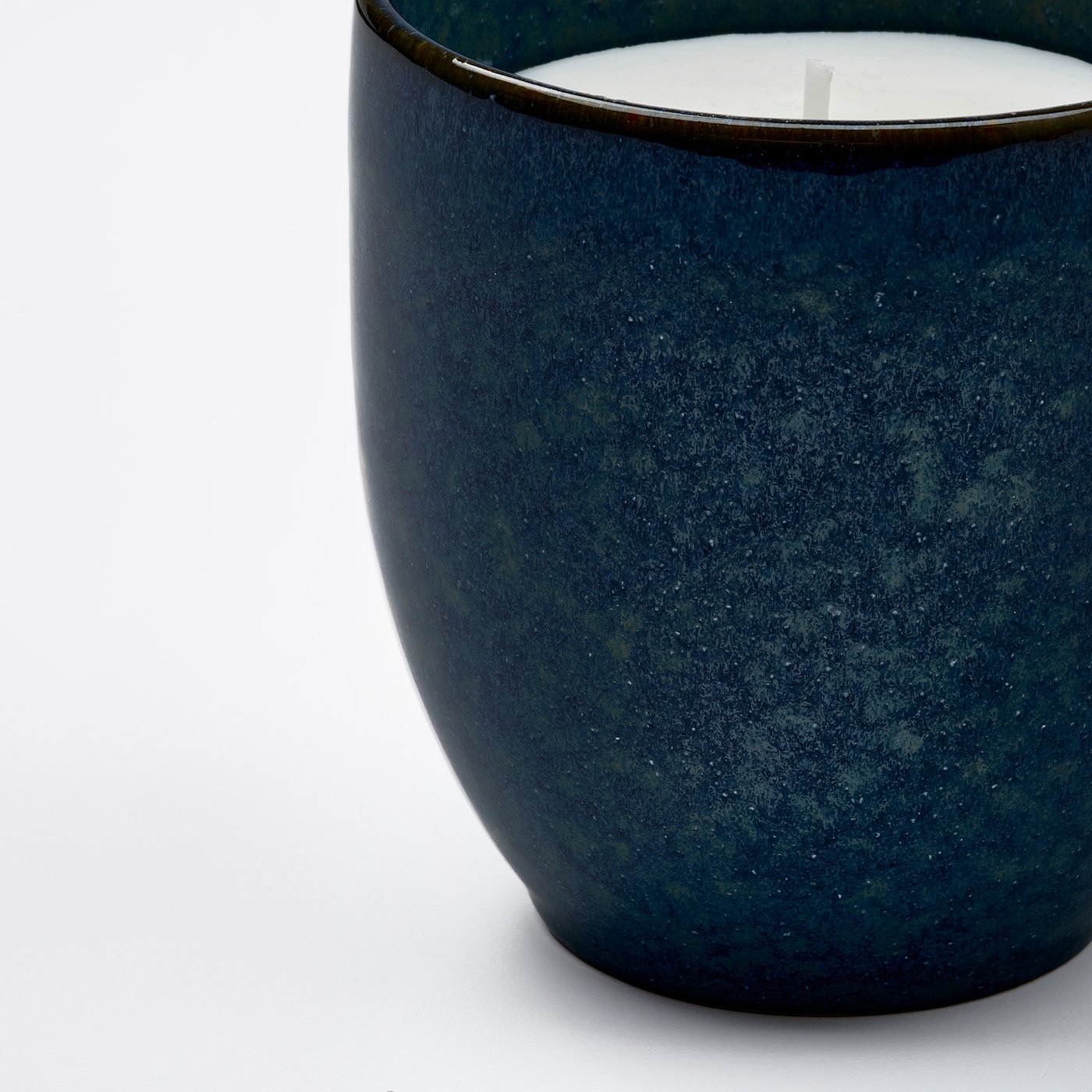 Close-up of a handcrafted, speckled blue-green stoneware candle with visible cotton wick.