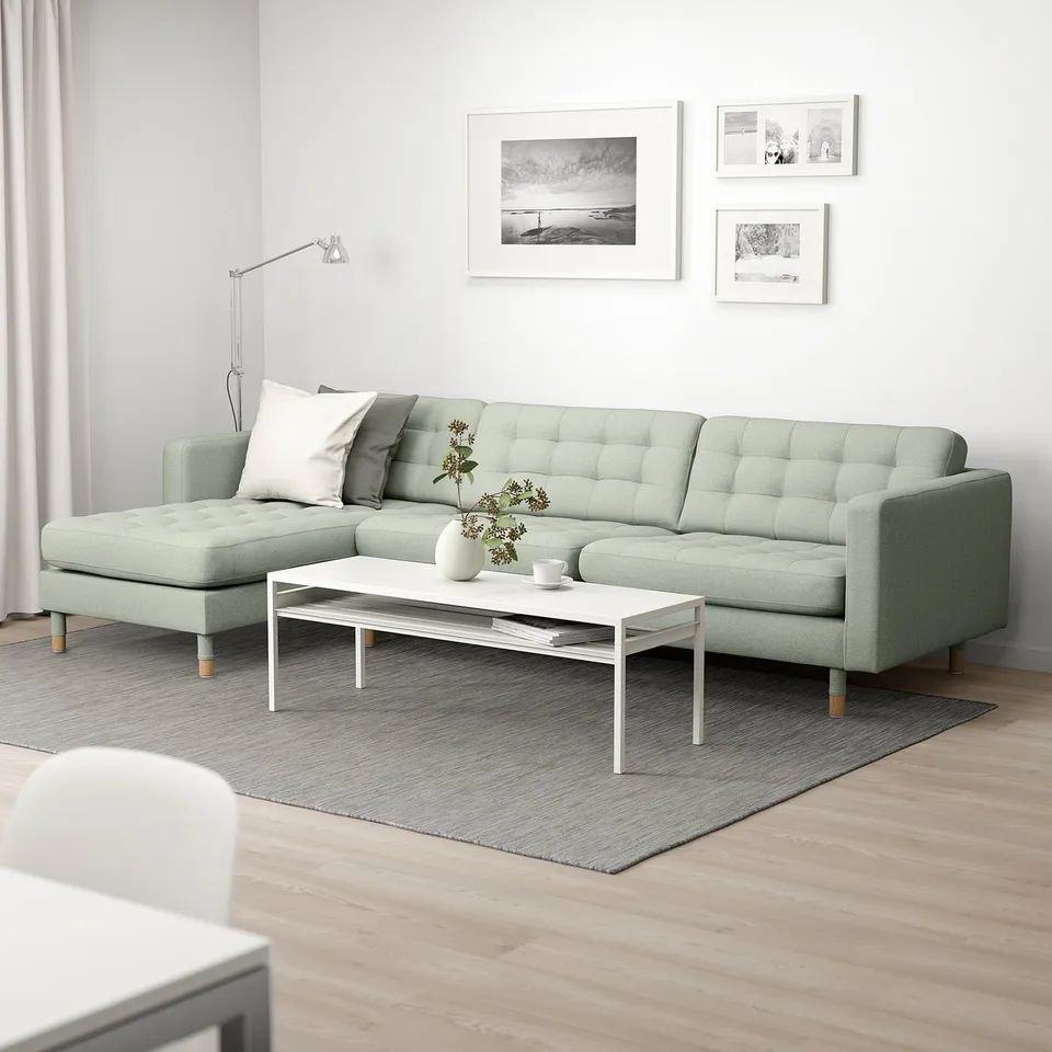 Modern living room with green sectional sofa, white coffee table, and rug. Cosy, minimalist setup with wall art and corner lamp.