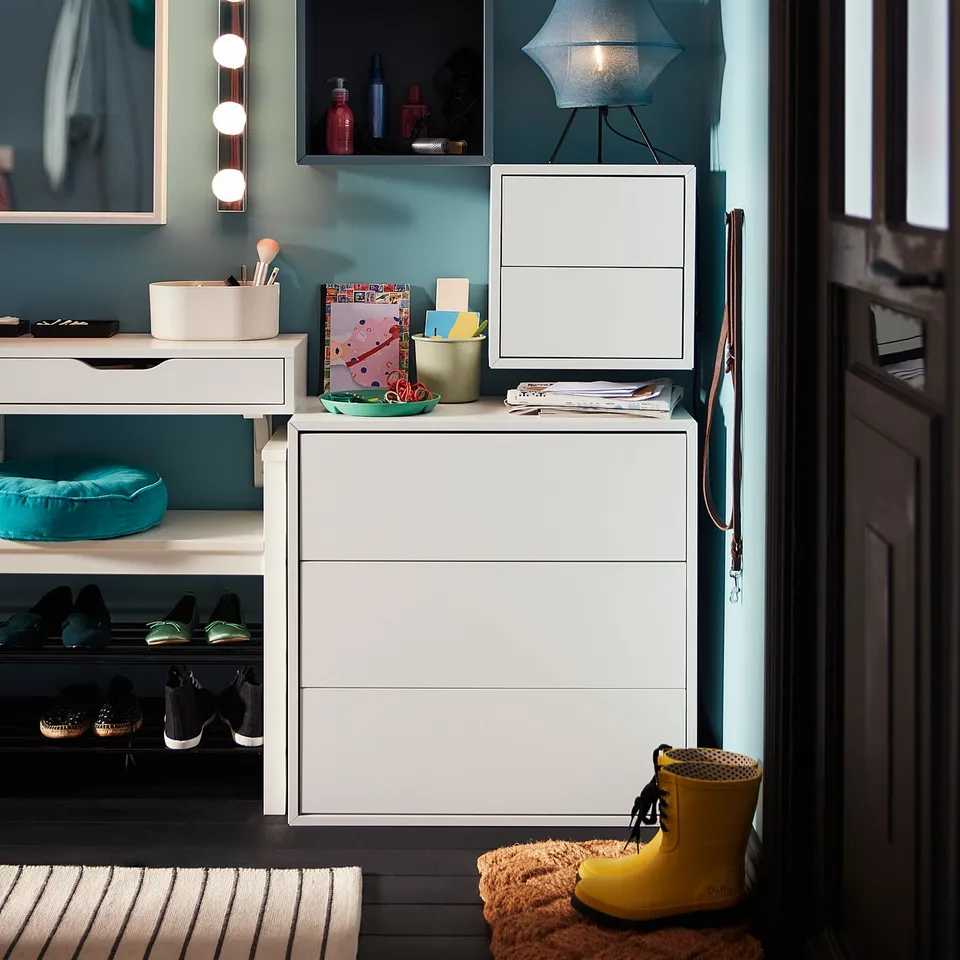 White EKET storage cabinet with blue accents; includes drawers, shelves, and hanging space. Modern design with teal wall.