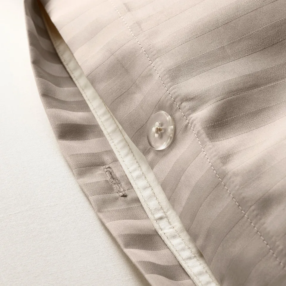 Close-up of striped sateen duvet cover with moisture-wicking fabric and a button for securing the duvet.
