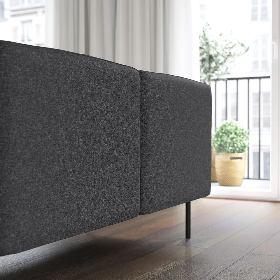 Black fabric sofa with high back, positioned near a window with plants, showcasing its modular design.