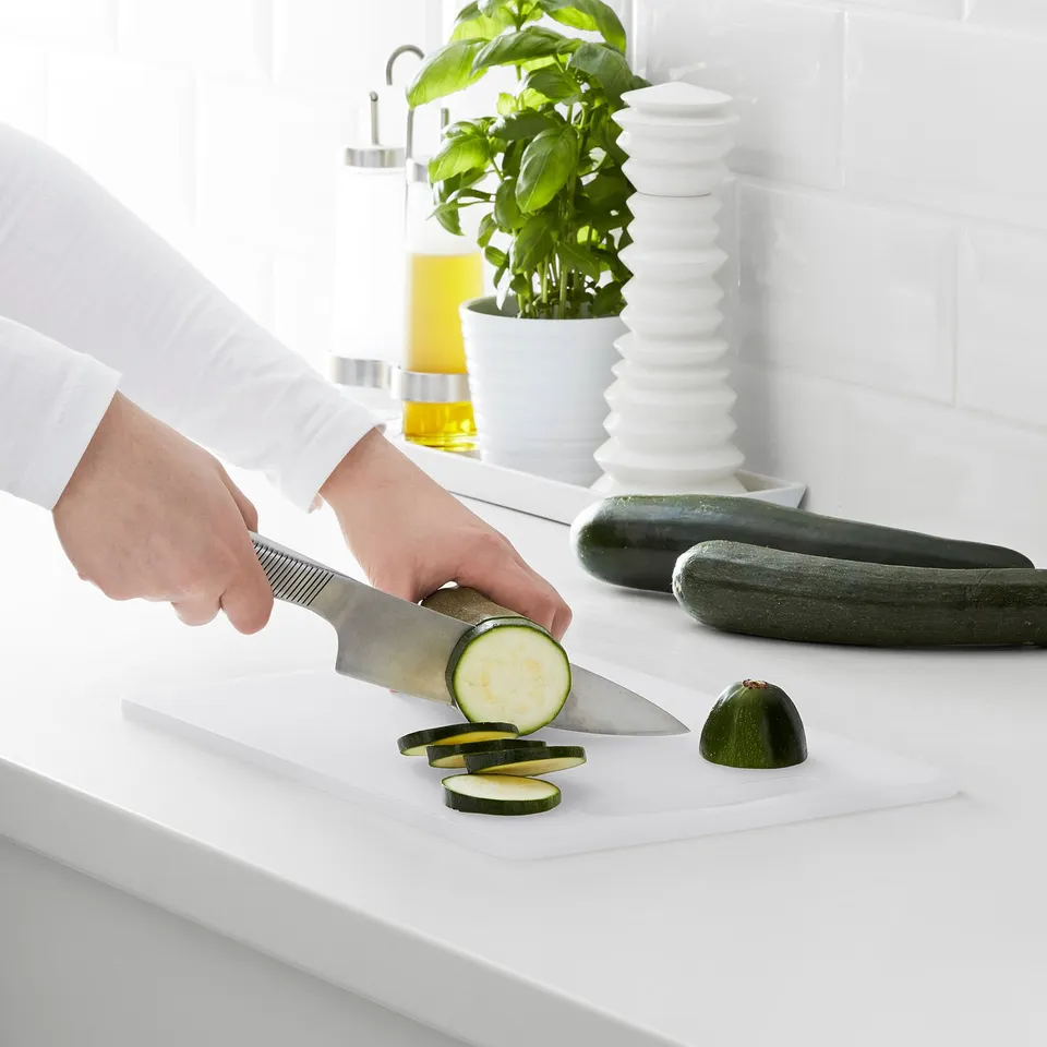 Person slices cucumber on white cutting board with a knife.