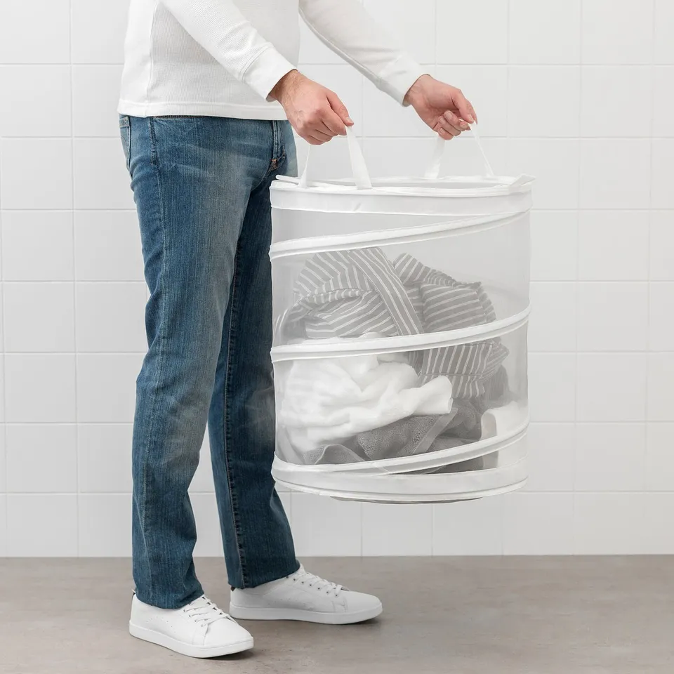 Person carrying a FYLLEN laundry basket with clothes, showcasing its breathable design and portability.