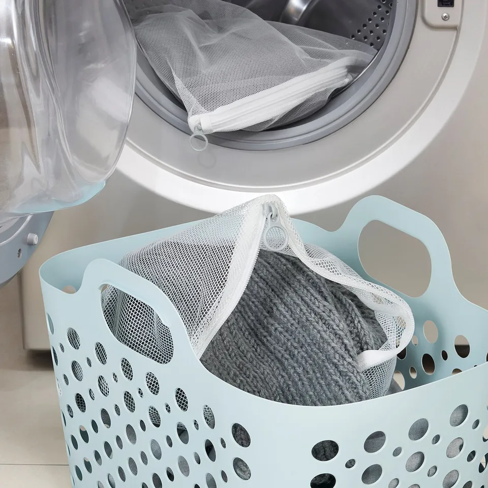 Mesh laundry bag with sweater beside open washing machine door.