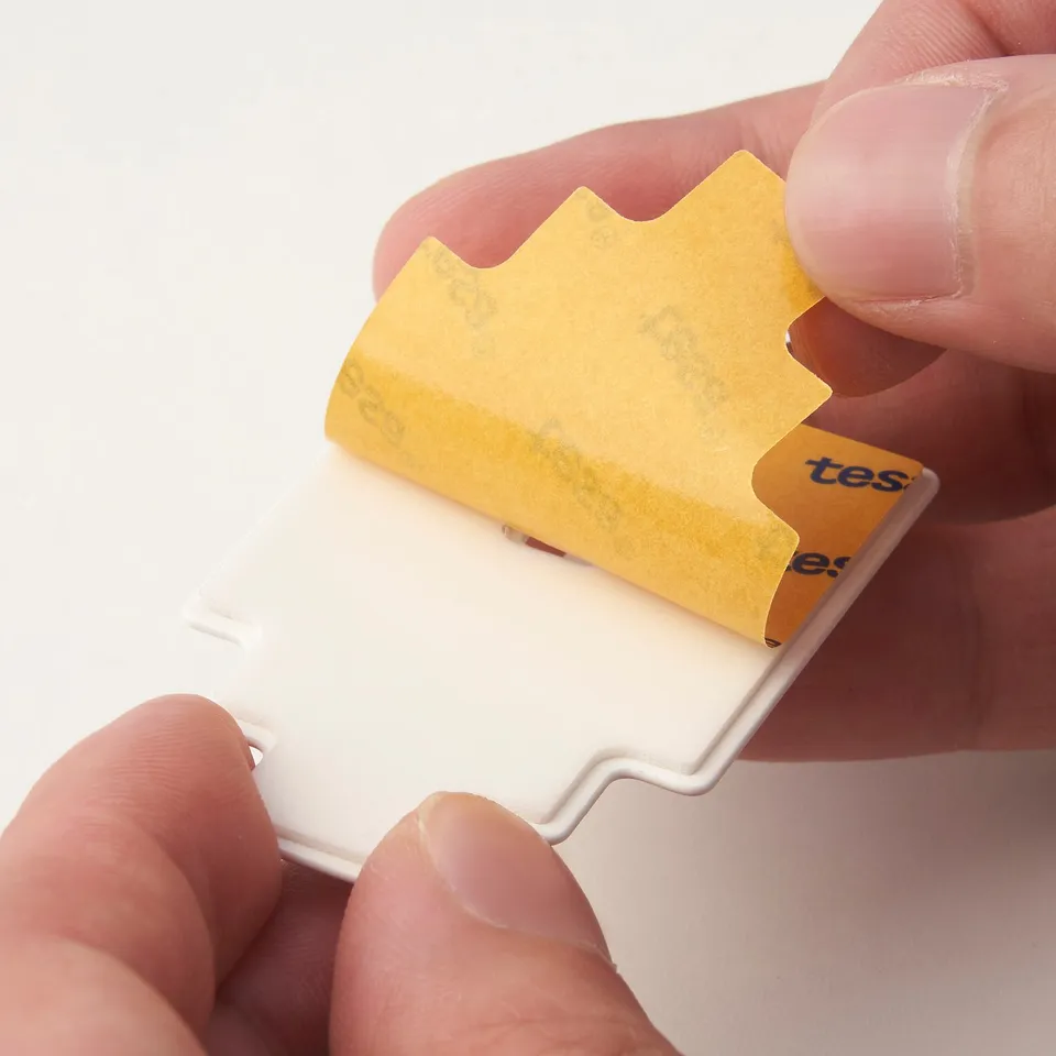 Hand holding a modern, minimalist-shaped metal hook, yellow protective film still on, indicating new and high-quality product.