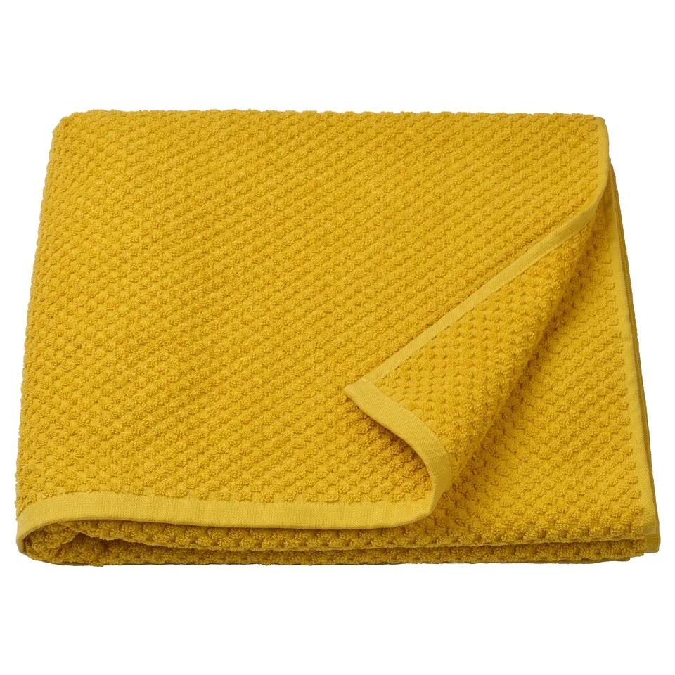A folded mustard yellow GULVIAL towel made of 100% cotton, thick and soft, rectangular shape.
