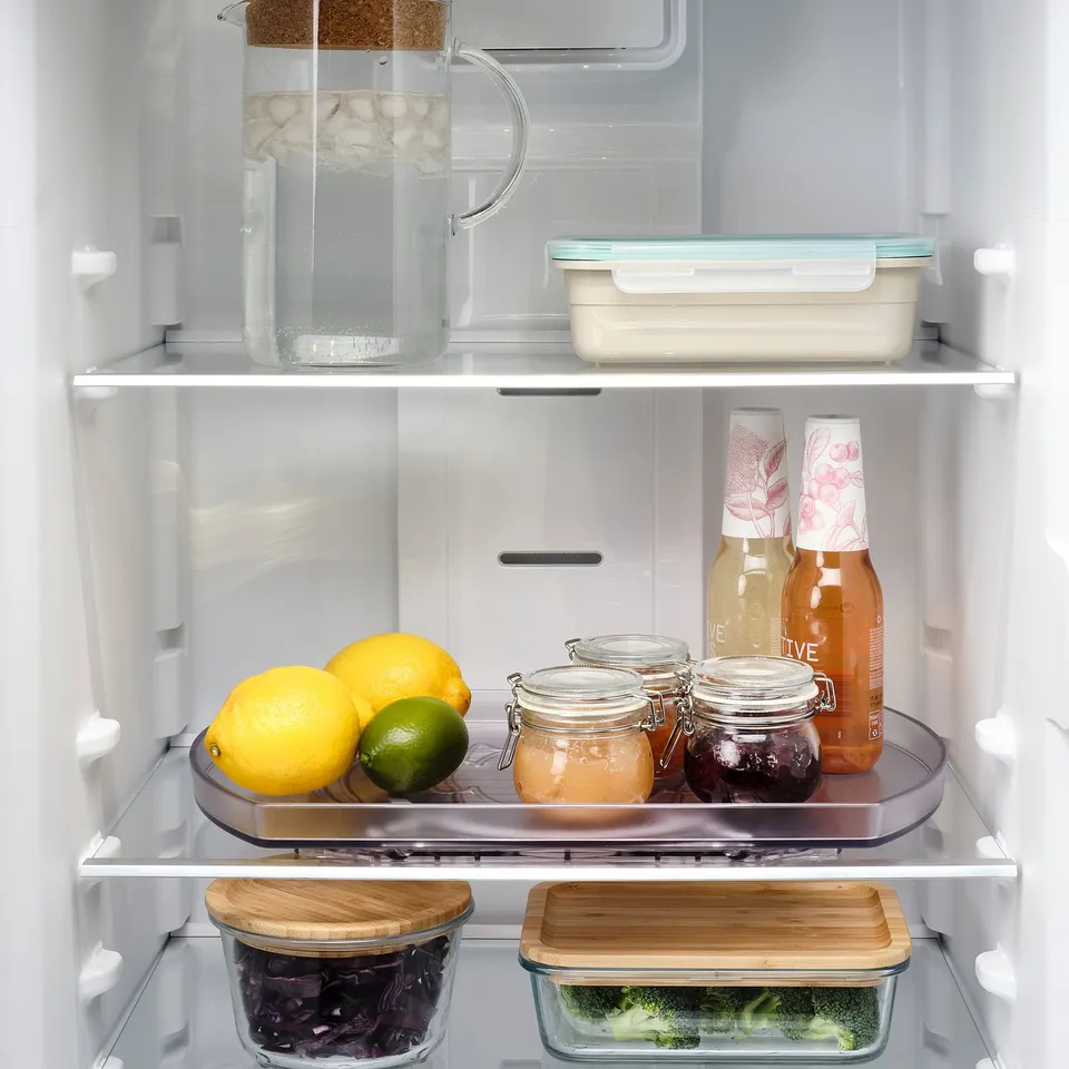 Open fridge with a revolving tray holding lemons, limes, jars, and bottles.