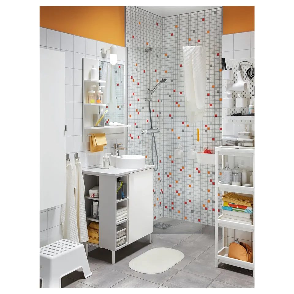 Bright bathroom with white tiles, colourful mosaic shower, white sink vanity, and organised storage shelves with various toiletries.