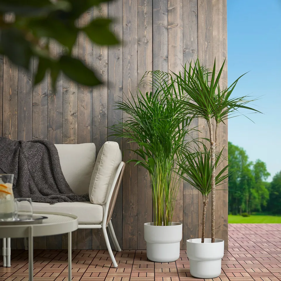 Cosy patio: two white FÖRENLIG plant pots holding green plants sit near a large armchair, on a wooden floor. Pots are small compared to the chair.