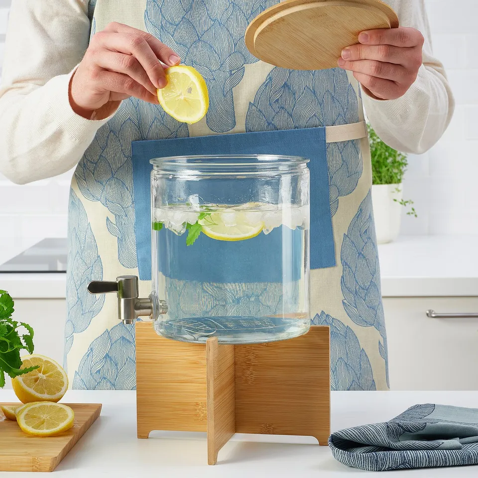 Person squeezing lemon into IKEA 365+ beverage dispenser with bamboo stand, filled with ice and mint.