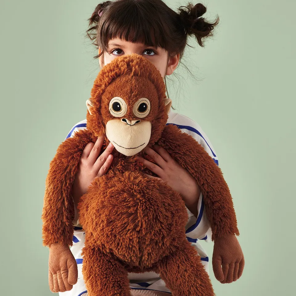 Girl holding toy orangutan with hangable hands and feet.