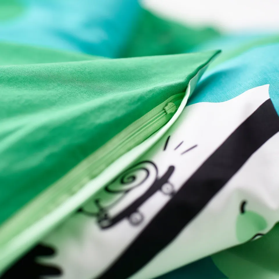 Close-up of soft, green bed linen with a playful tree print, showing zip detail and elastic edge for safety.
