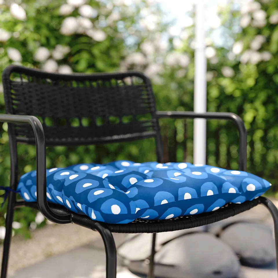 Black chair with blue polka dot cushion outside, overlooking greenery.