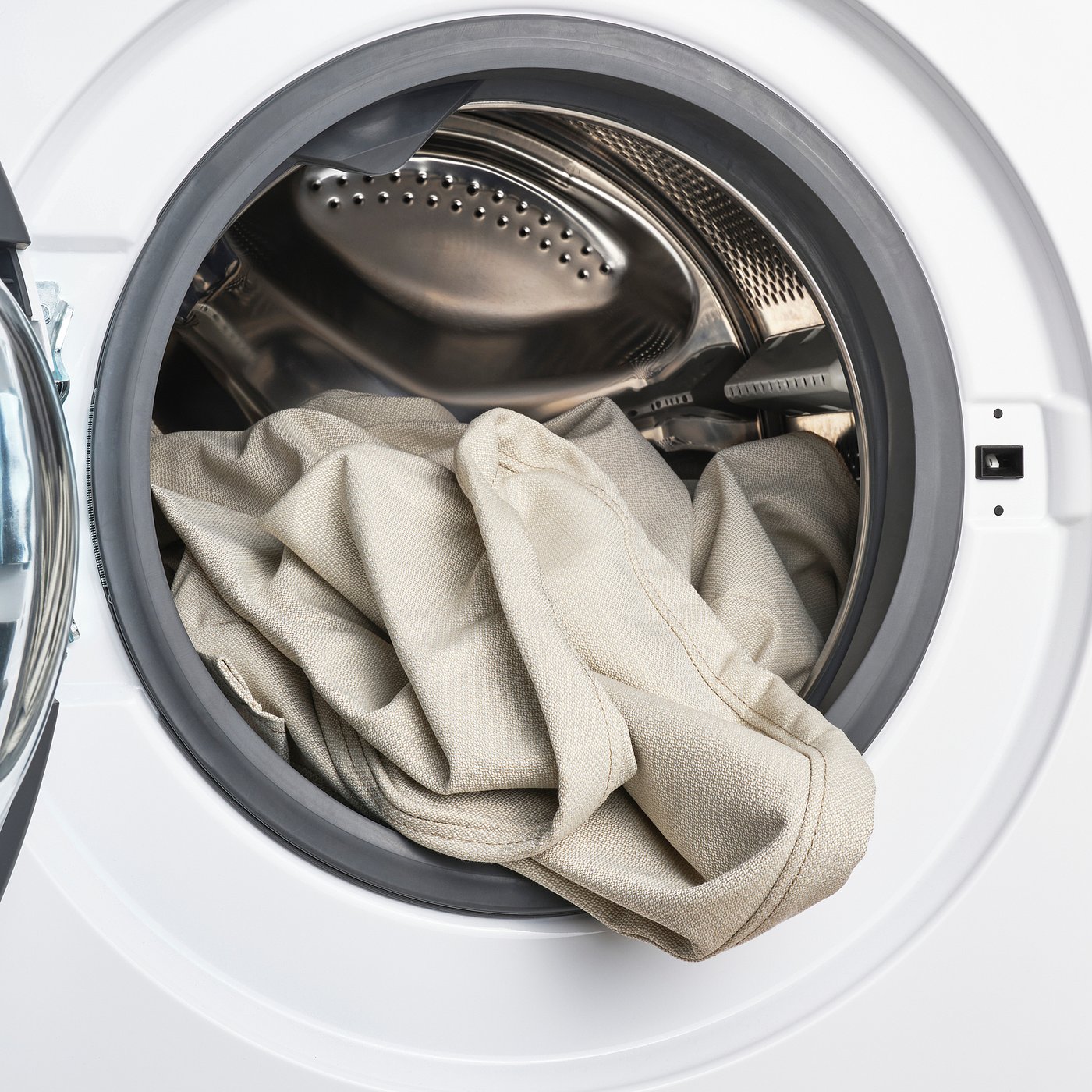 Washing machine door open, showing load of light-colored fabric inside.