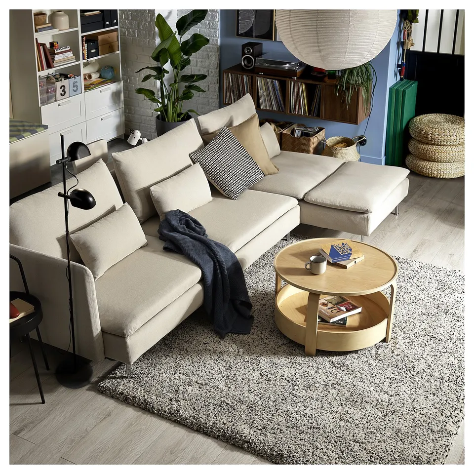 Modern cream-colored l-shaped sofa bed in cosy living room with wooden coffee table, rug, and plants.