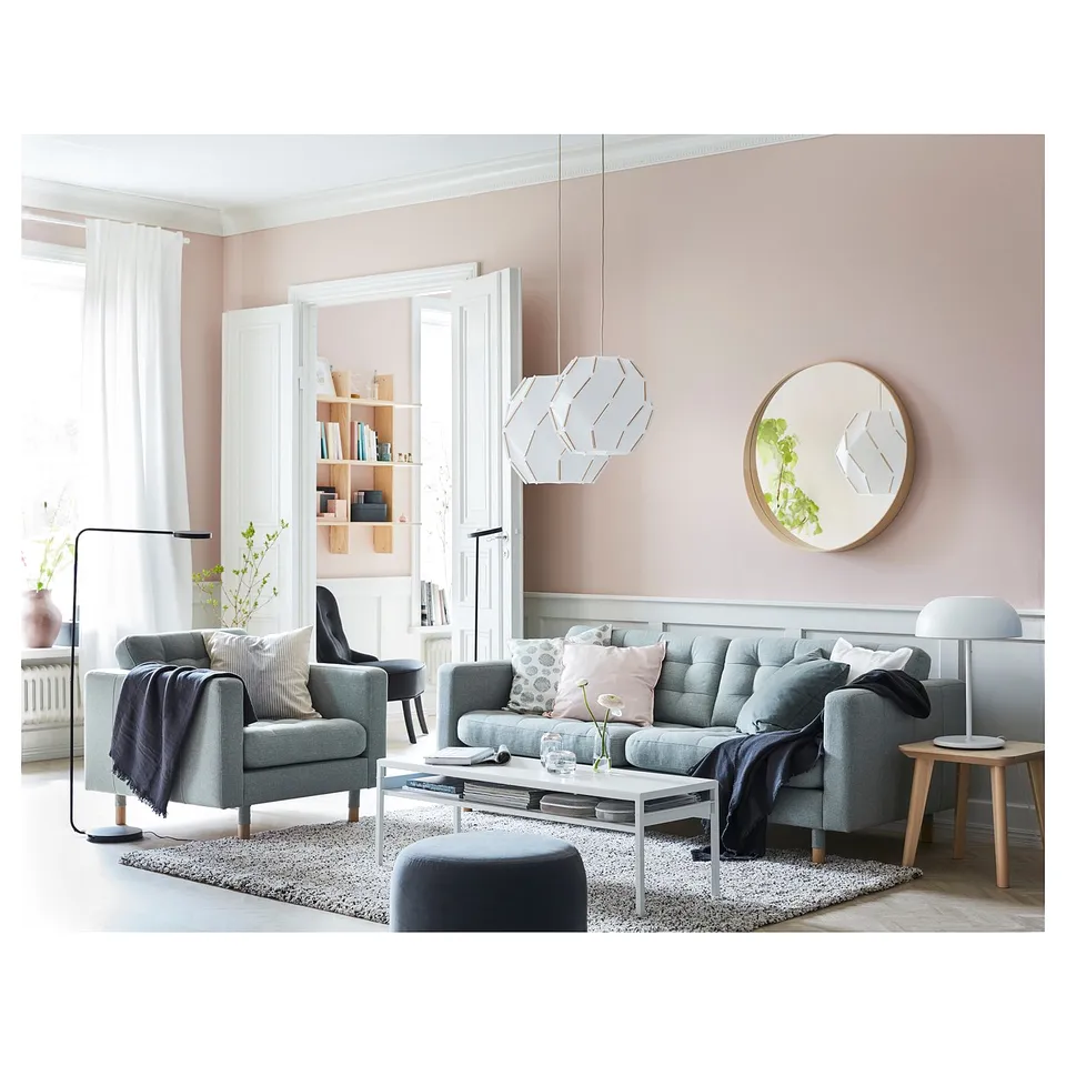 Modern living room with pink walls, a greylandskröna sofa, coffee table, lamp, and round mirror.
