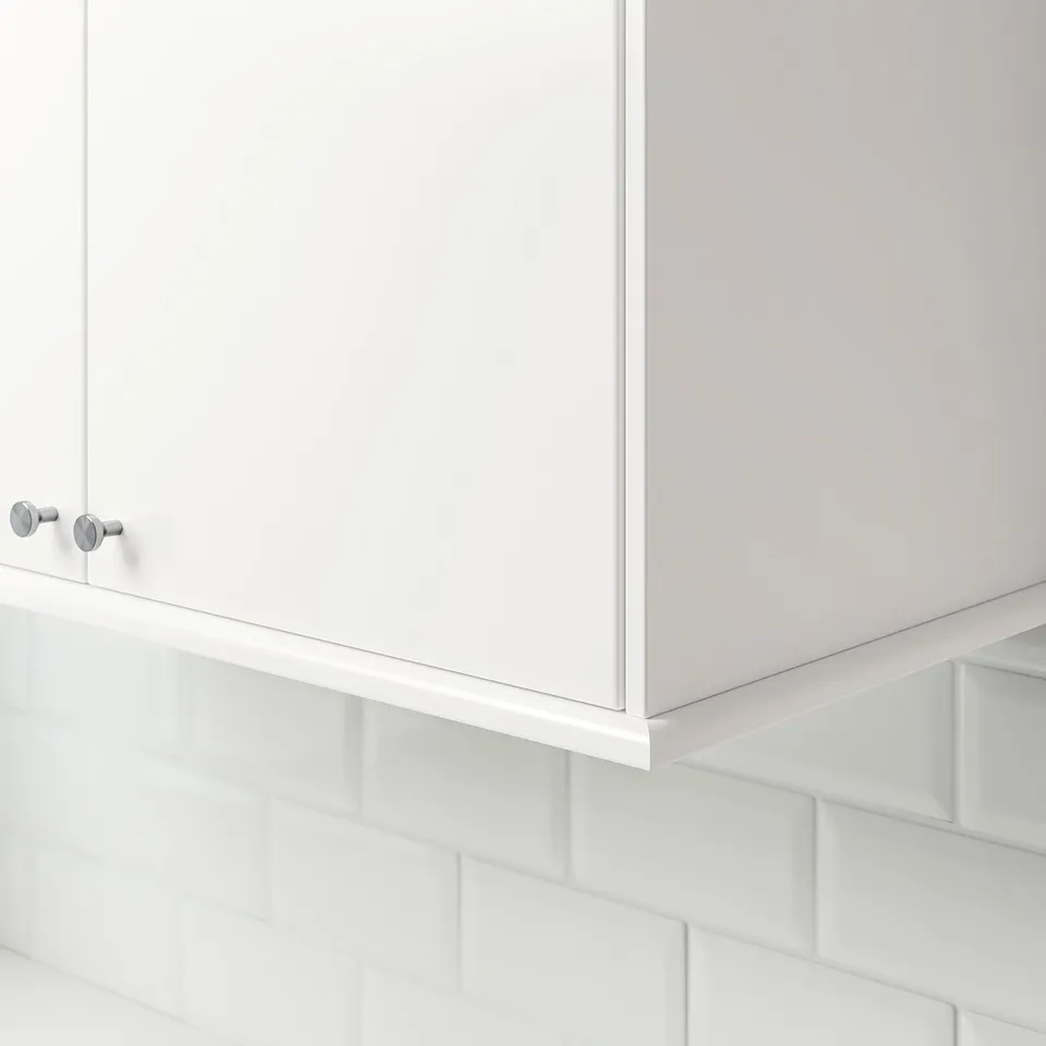 White kitchen cabinet trim, two silver knobs visible, mounted on white subway tiled wall.