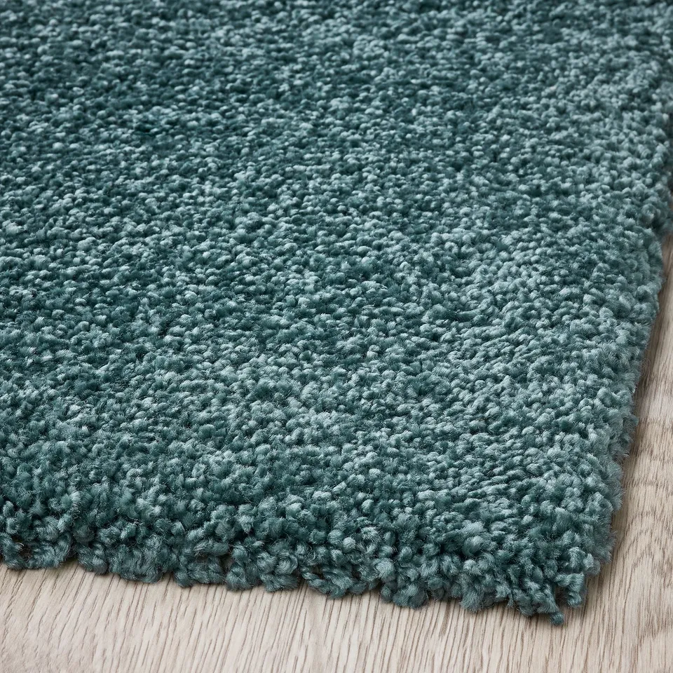 Shaggy green rug on wooden floor. Thick, soft pile, sheen varies.