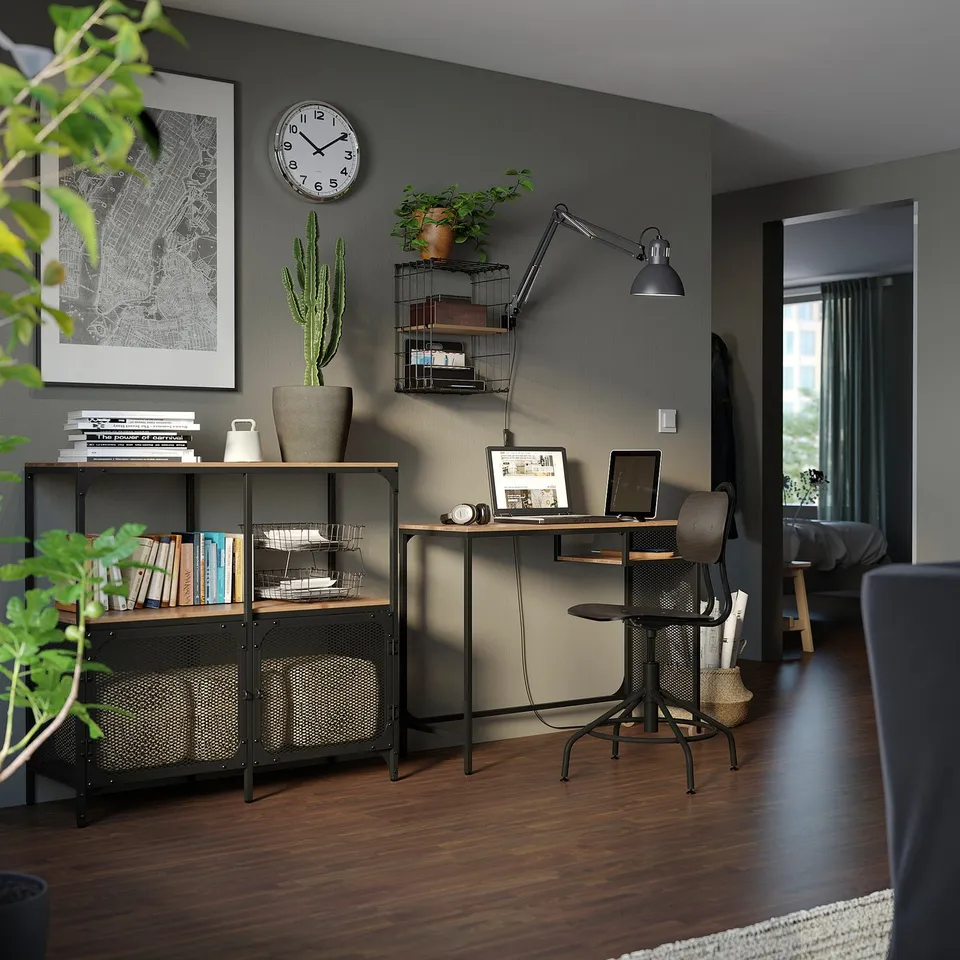 Modern home office with dark walls, wooden floors, & FJÄLLBO shelving. Desk, chair, books, plants, decor.
